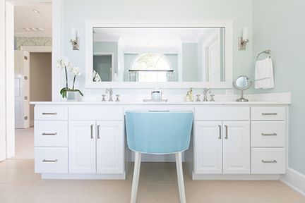 White bathroom vanity with blue chair, large mirror, and light blue walls.