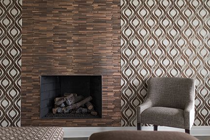 Fireplace with wood-look tile, patterned wallpaper, and a gray armchair.