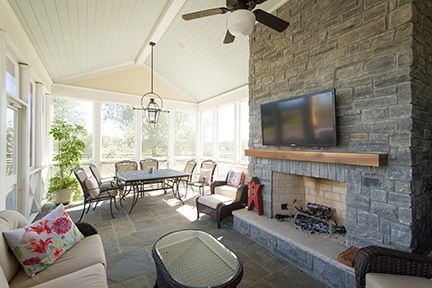Sunroom with stone fireplace, TV, seating, dining table, and a ceiling fan.