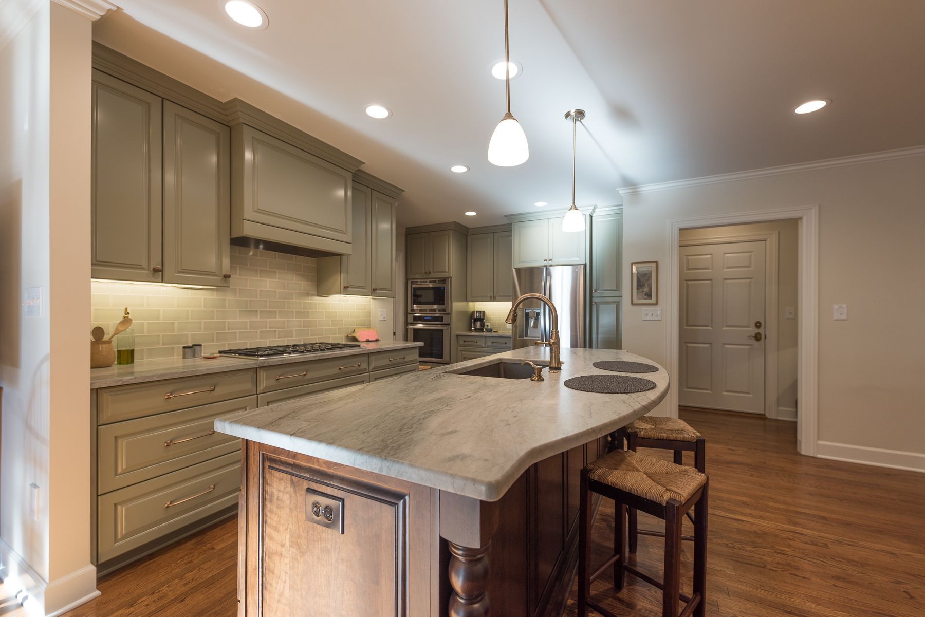 Kitchen with gray cabinets, marble island, wooden floor, and two pendant lights.