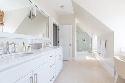 White, bright bathroom with double vanity, shower, and sloped ceiling.