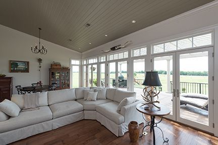 Spacious living room with white sectional, large windows overlooking a field, and wooden floor.