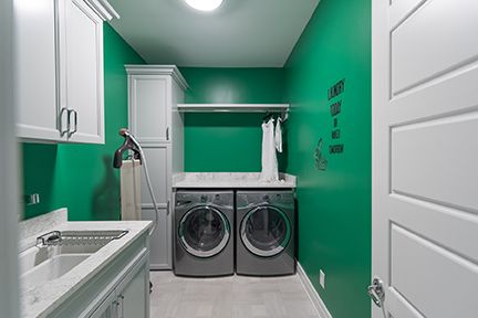Green and white laundry room with washer, dryer, cabinets, and drying rack.
