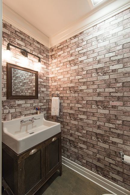 Small bathroom with brick-patterned wallpaper. Sink and cabinet are dark wood. Mirror, light fixture, and towel ring are black.