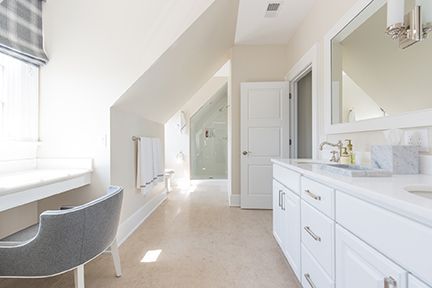 Bright white bathroom with vanity, shower, and towel rack. Angled ceiling. Gray chair.