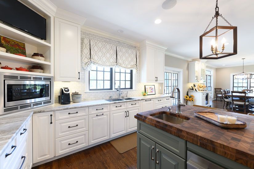 White kitchen with island, wood countertops, window, and built-in appliances.