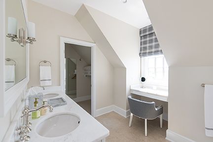 Bathroom with white vanity, double sinks, and a small desk under a slanted window with a plaid shade.