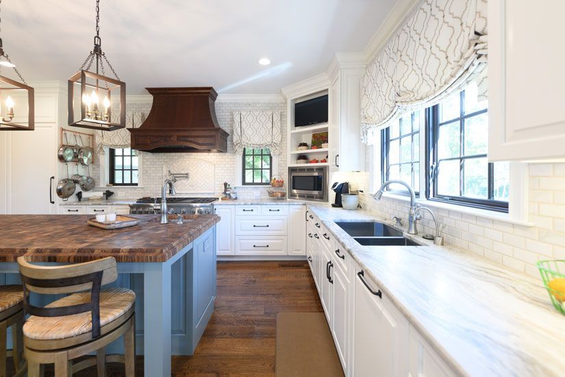 Elegant white kitchen with blue island, wood cabinets, and dark bronze light fixtures.