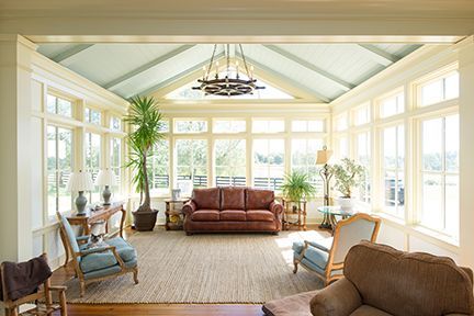 Sunroom with sofa, chairs, plants, and large windows; natural light, neutral colors.