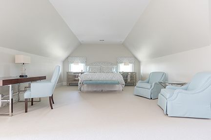 Bright bedroom with light blue accents; bed, chairs, and desk under a vaulted ceiling.