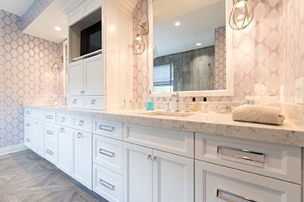 White bathroom vanity with marble countertop, silver hardware, patterned wallpaper, and a large mirror.