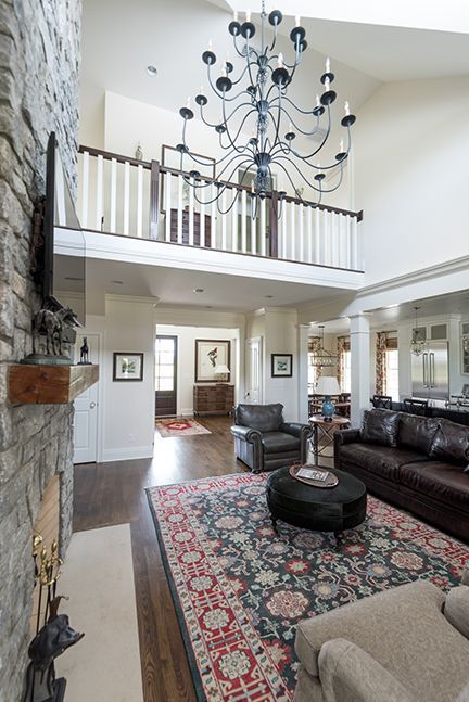 Living room with stone fireplace, dark leather furniture, large chandelier, and ornate rug.