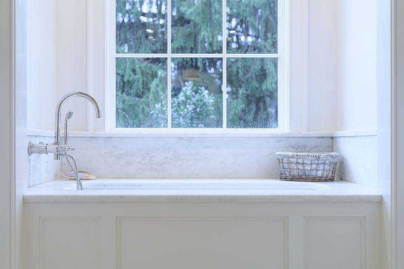 White built-in bathtub under a window, with a faucet and small basket. View of trees through the window.