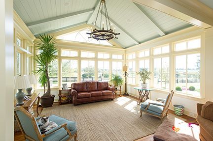 Sunroom with brown leather sofa, blue chairs, large windows, and light green ceiling.