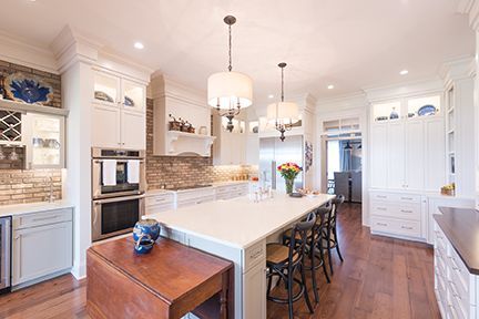 Spacious white kitchen with large island, wood floors, and brick backsplash.