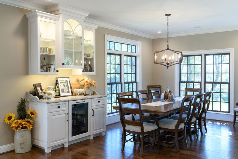 Dining room with a white cabinet, table set for guests, and large windows.