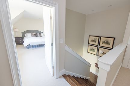 Hallway with stairs leading down, open doorway to bedroom. Light walls, neutral colors, framed artwork.
