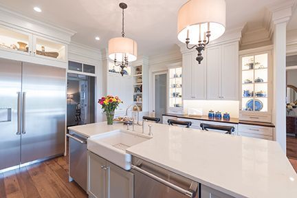 Elegant white kitchen with stainless steel appliances, large island, hardwood floors, and pendant lights.
