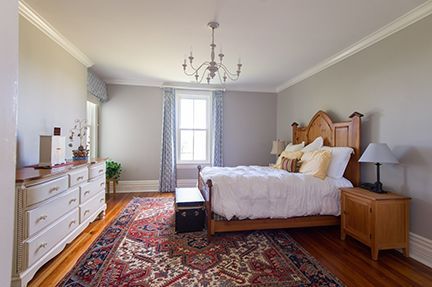 Bedroom with wooden furniture, white bedspread, patterned rug, and chandelier.