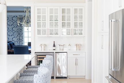White kitchen with bar area; wine cooler, cabinets, and chairs with blue patterned fabric.