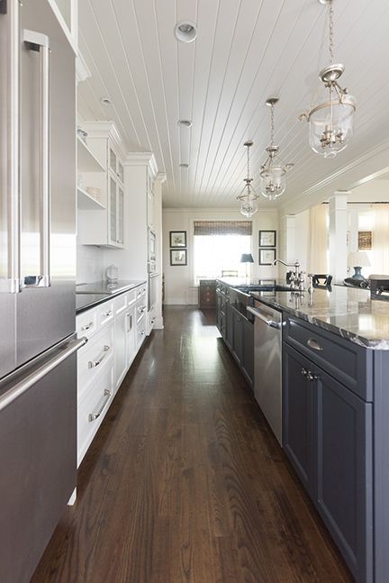Modern kitchen with white cabinets, dark blue island, stainless steel appliances, and wood floors.