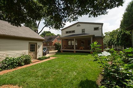 Backyard with grass, a garage on the left, and a two-story house with a porch on the right.