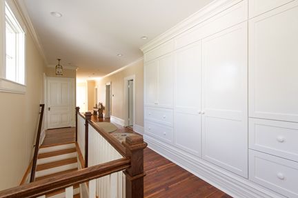 Hallway with stairs, built-in white cabinets, and hardwood floors. Wooden railing on the left.