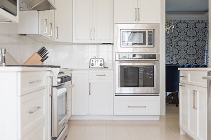 White kitchen with stainless steel appliances and cabinets, and patterned blue wallpaper.