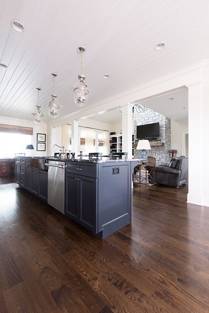 Dark-blue kitchen island with stainless steel appliances, hardwood floor, connected to a living room with a stone fireplace.