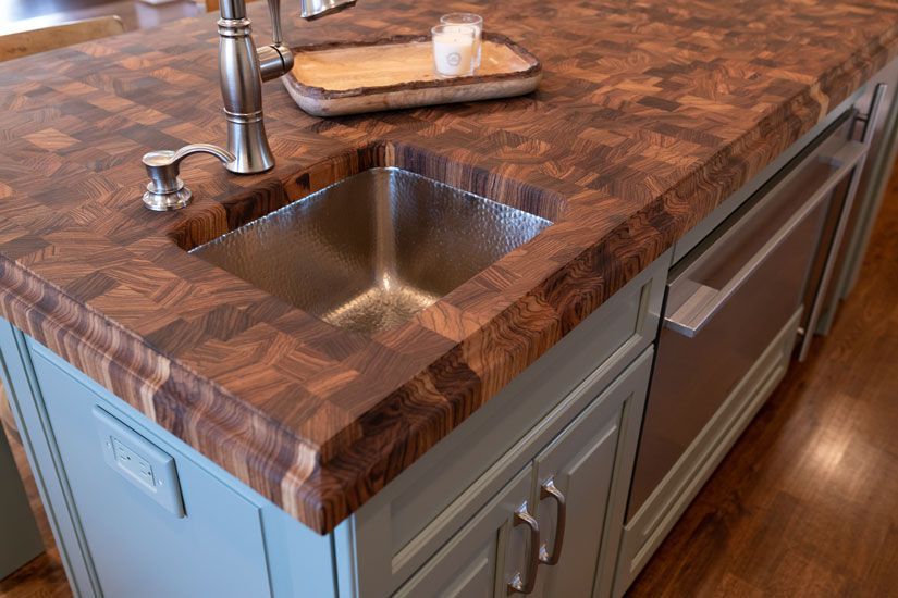 Kitchen island with wooden butcher block countertop, stainless steel sink, and light blue cabinetry.