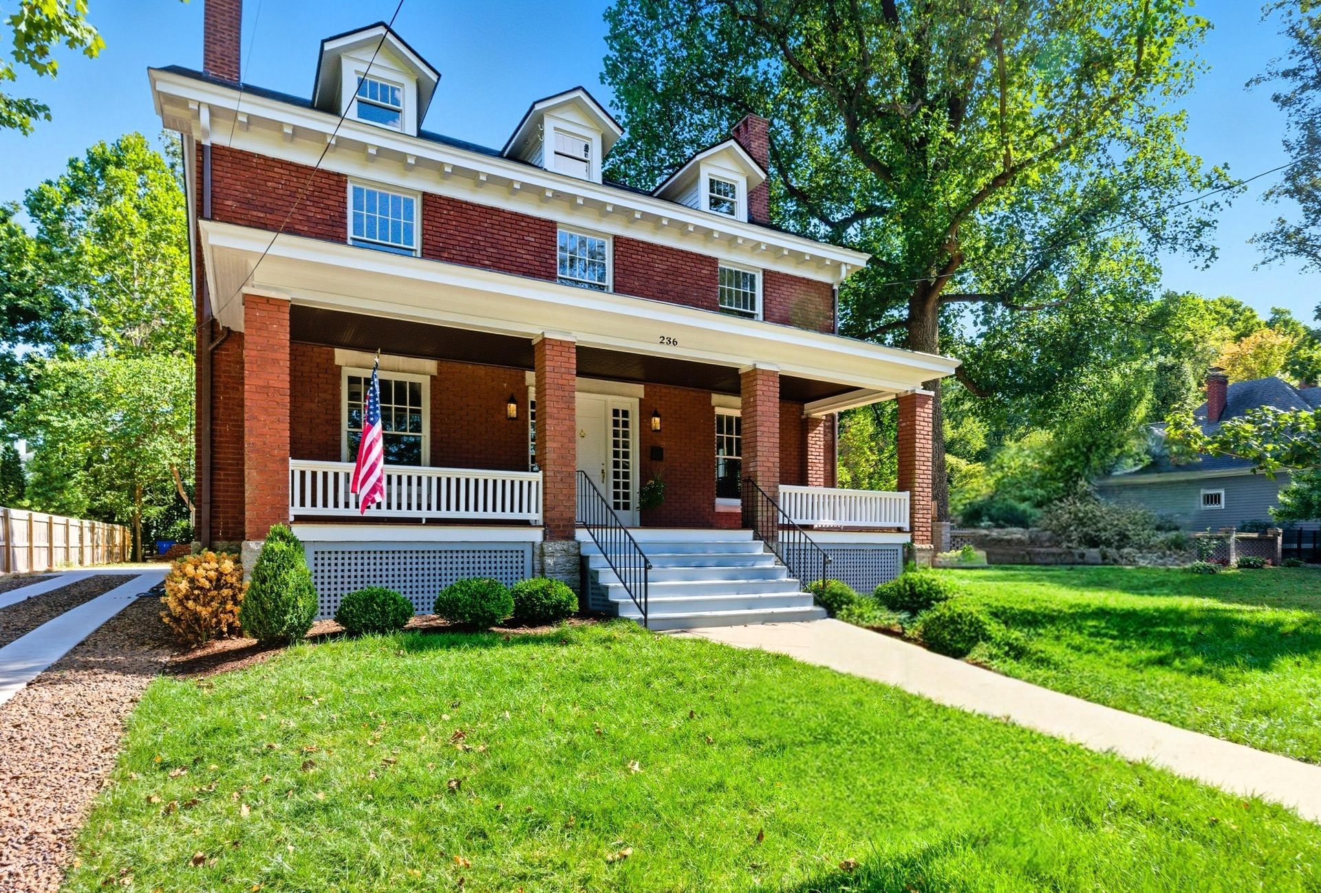 Brick two-story house with porch, flag, white trim, green lawn, and driveway. Sunny day.