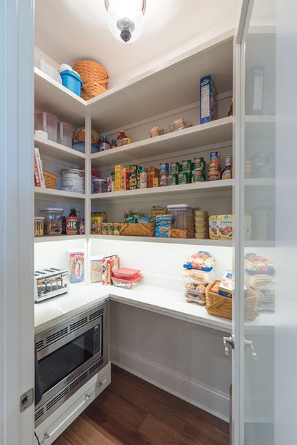 White pantry with shelves of food, including a microwave and toaster on counter.