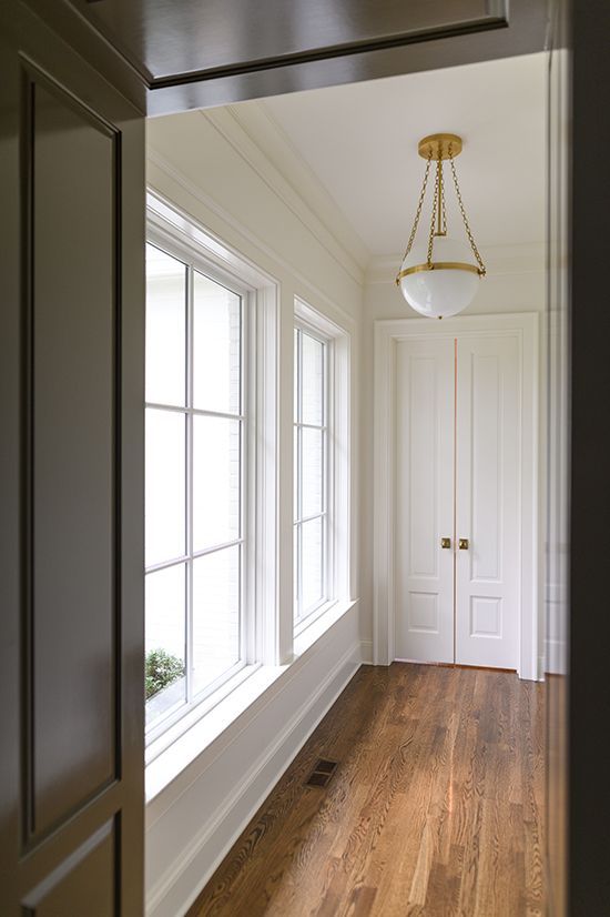 Bright hallway with wood floor, white walls, windows, and a gold pendant light.