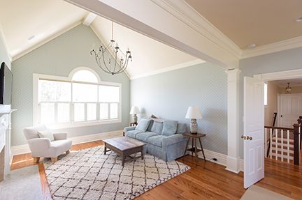 Living room with high ceiling, light blue walls, wooden floor, and a rug.