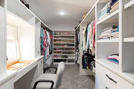 Walk-in closet with white shelves, hanging clothes, shoes, and a desk with a chair.