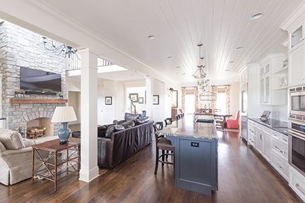 Spacious, open-concept living space with a stone fireplace, modern kitchen, dark wood floors, and a large leather sofa.