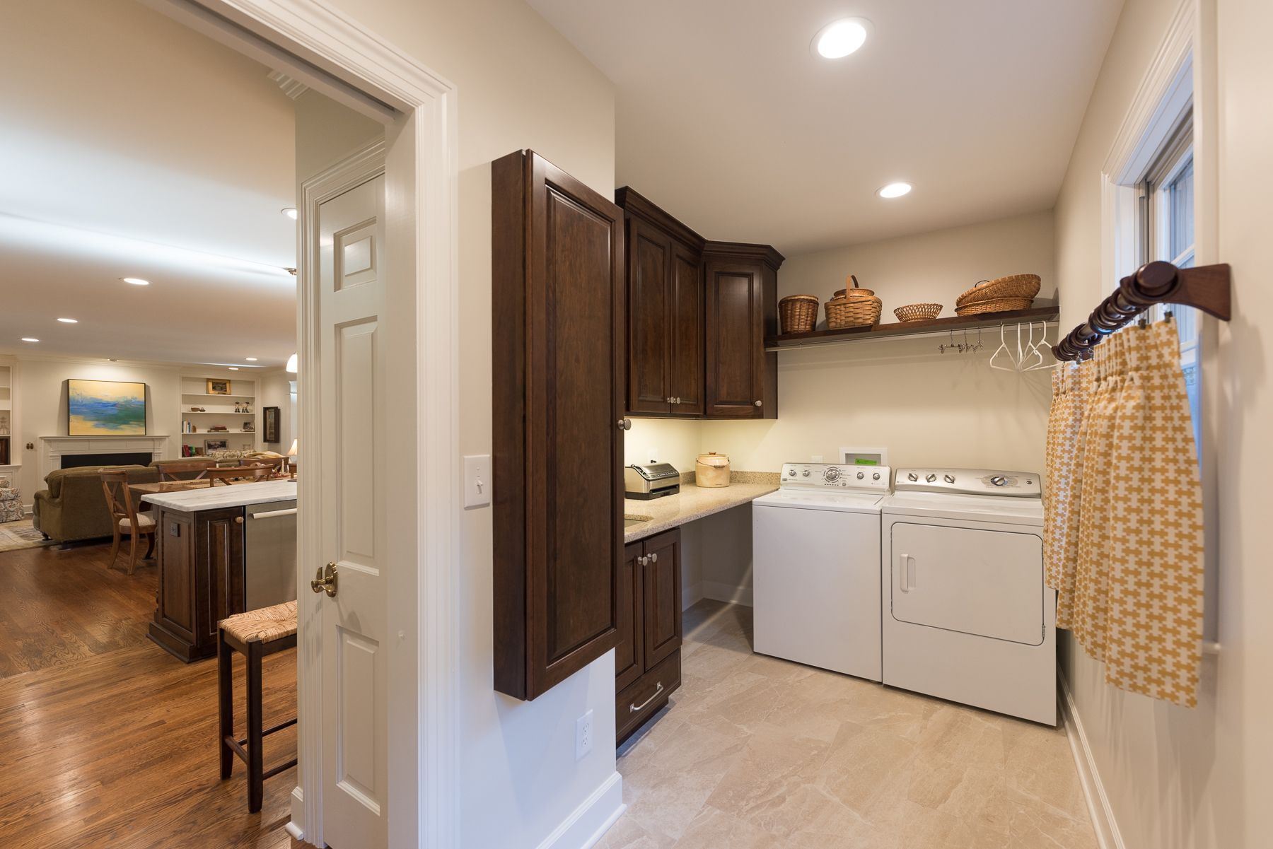 Laundry room with washer, dryer, cabinets, and counter. Adjacent to a kitchen/living area with hardwood floors.