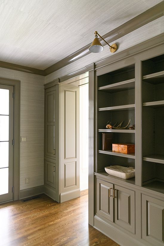 Built-in gray bookshelves with a hidden door and wood flooring, featuring a brass wall sconce.