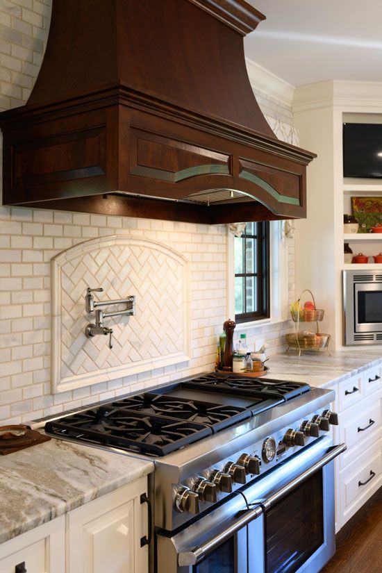 A kitchen with a stainless steel stove, wooden range hood, and marble countertops.