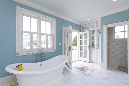 Blue-walled bathroom with a white claw-foot tub, open doors to the outdoors, and a white window.