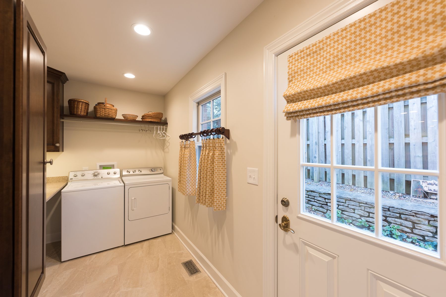 Laundry room with a washer, dryer, cabinets, window with a shade, and a door.
