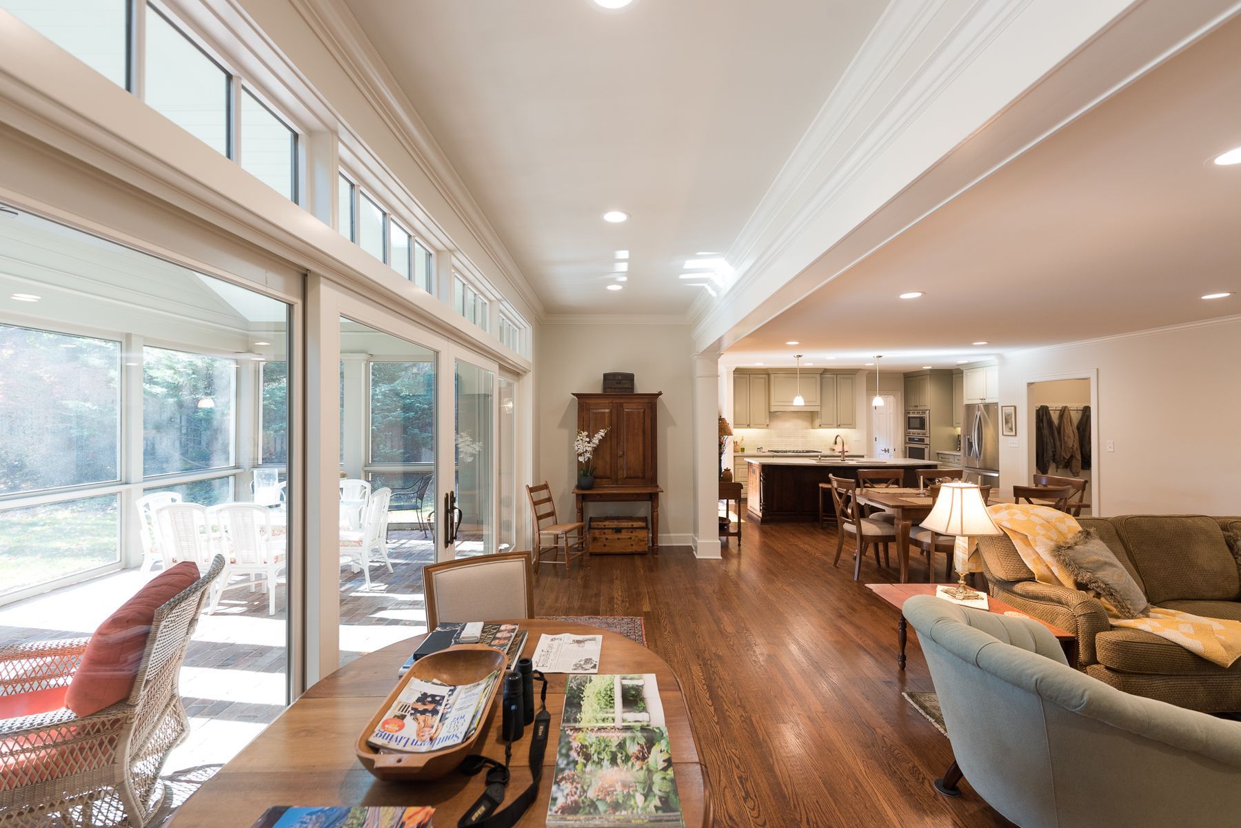 Open-plan living area with patio access; features wood floors, light walls, and furniture. Kitchen visible in the background.