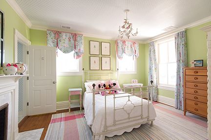 A girl's bedroom with green walls, floral curtains and bedding, white furniture, and a chandelier.