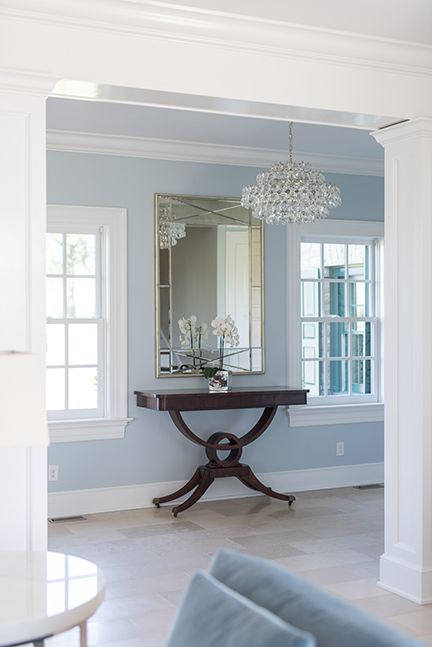 Elegant entryway with a dark wood table, large mirror, and chandelier against a light blue wall.