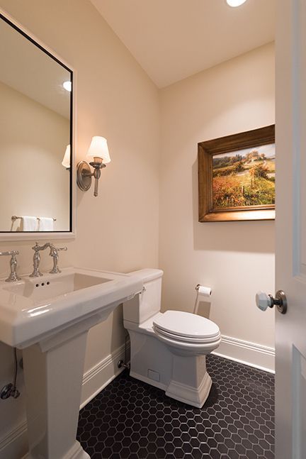 Small powder room: white pedestal sink, toilet, black hexagon tile floor, artwork, mirror, and sconce.