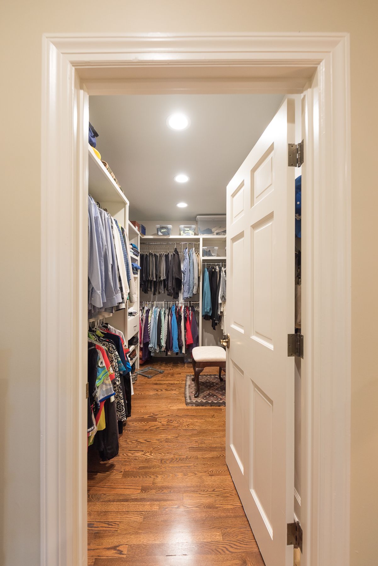 Open doorway leads to a well-lit walk-in closet filled with hanging clothes on wooden floor.