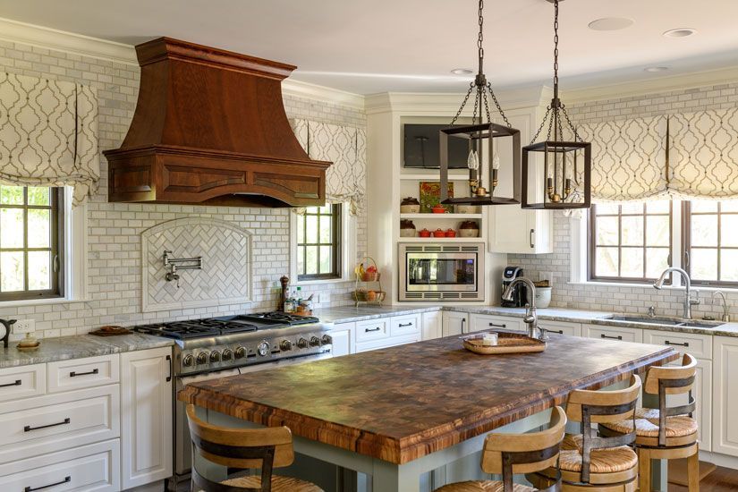 A kitchen with white cabinets, wooden island, and a dark wooden range hood.
