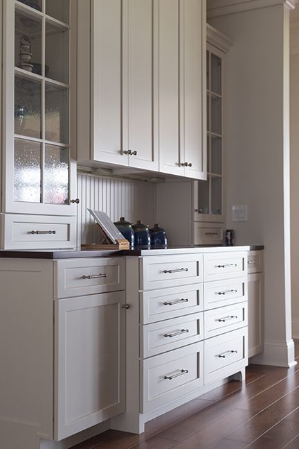 White kitchen cabinets with drawers and glass-front display, hardwood floors.