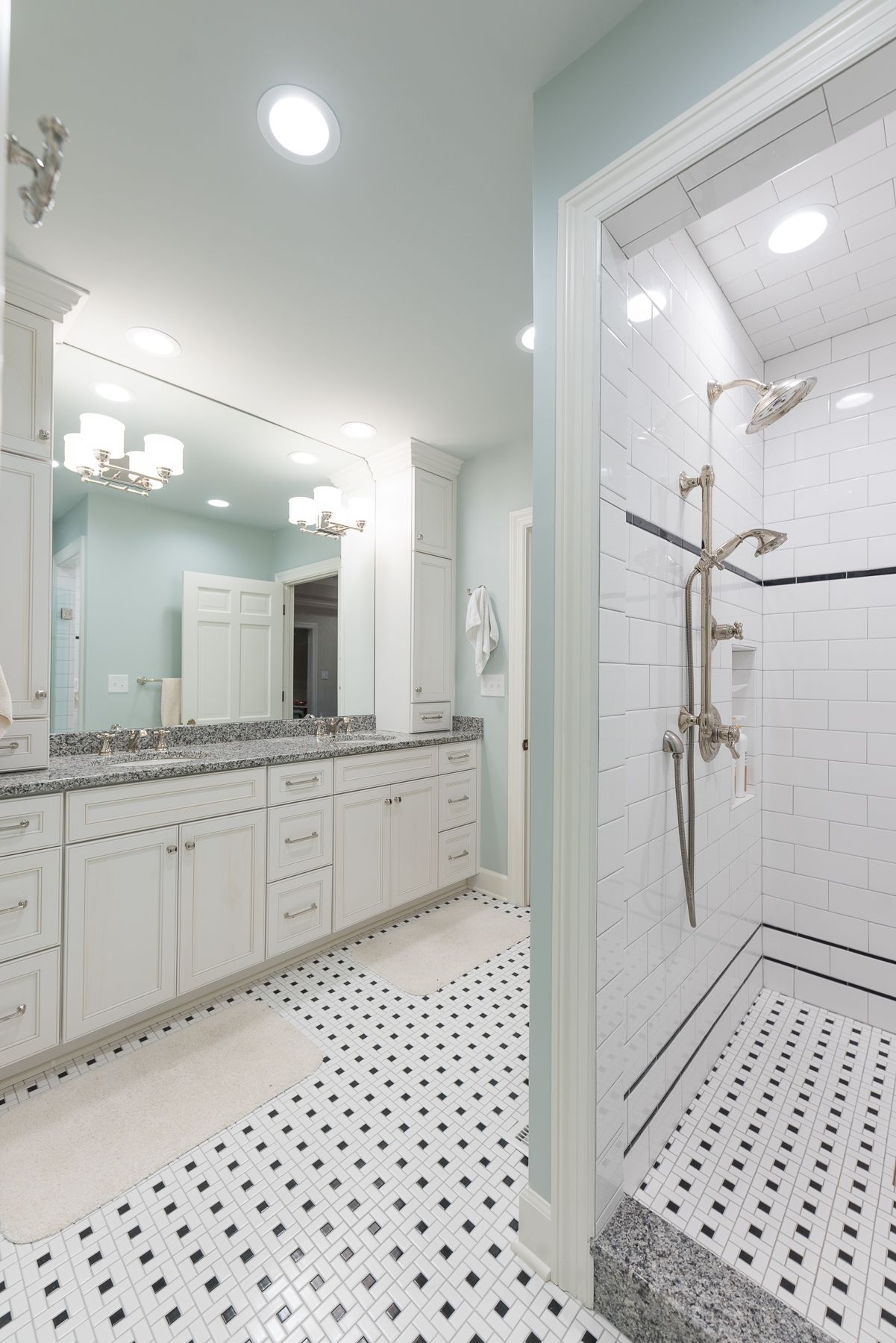 Bathroom with white cabinets, black and white tiled floor, and a shower with white subway tile.