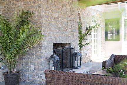Stone fireplace with lanterns, wicker furniture, and palm trees on a covered patio.